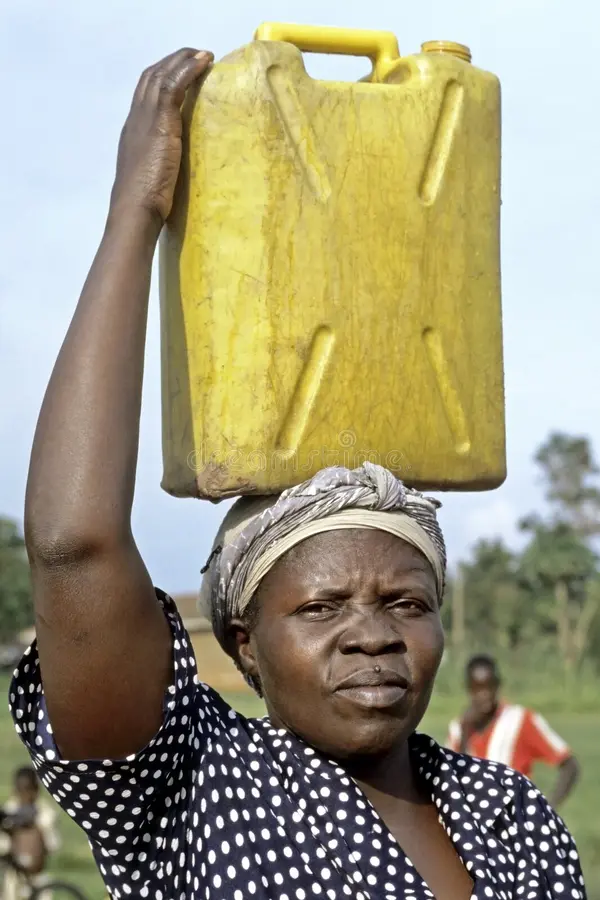 A local woman carrying a yellow jerrycan on her head while walking up a steep mountain trail in Mbale.