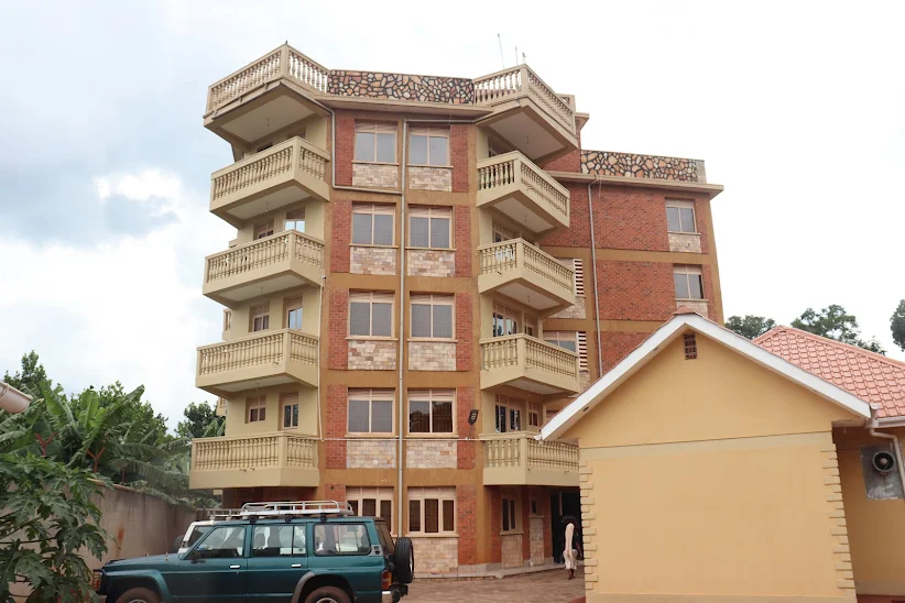 The multi-story exterior of Jusvero Motel in Jinja, featuring earth-toned brickwork, stone accents, and several tiers of private balconies with classic balustrades under an overcast sky.