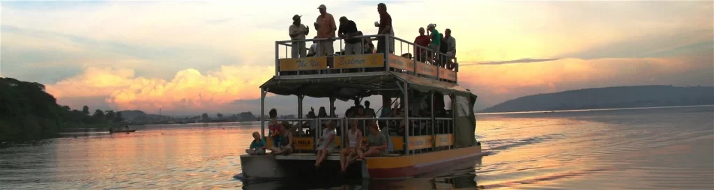 A double-decker tourist boat named The Nile Explorer filled with people on the river at sunset.
