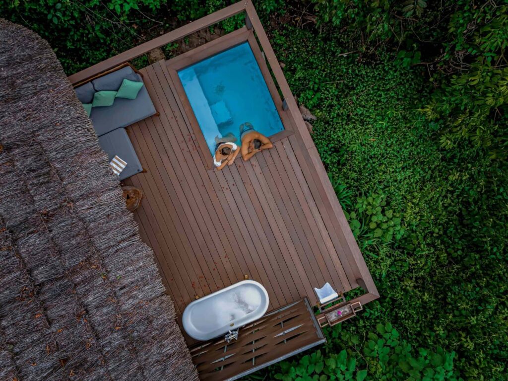 Lemala Wild Waters Lodge Jinja: The Ultimate Private Island Retreat. Aerial drone view of a private timber deck at Lemala Wild Waters Lodge, featuring a plunge pool and free-standing outdoor bathtub overlooking the Nile riverine forest on Kalagala Island.