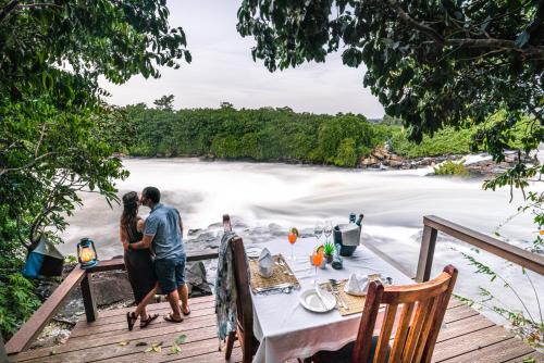 Lemala Wild Waters Lodge Jinja: The Ultimate Private Island Retreat. A private, candle-lit dinner for two on a secluded timber deck at Lemala Wild Waters Lodge, featuring a formal table setting with a cinematic view of the churning Nile rapids.