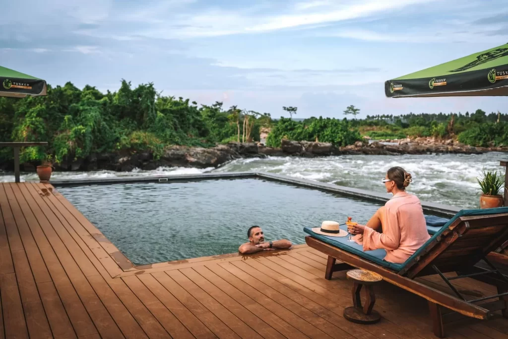 Lemala Wild Waters Lodge Jinja: The Ultimate Private Island Retreat. Guests enjoying cocktails and relaxation at the Lemala Wild Waters infinity pool, with a clear view of the white-water rapids on the River Nile at Kalagala Island.