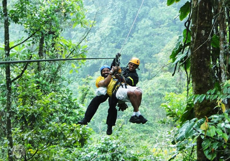 Two people ziplining through a dense green rainforest canopy in Mabira Forest.