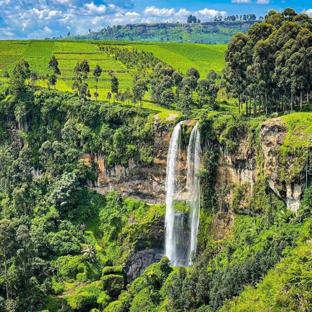 A high-altitude view of the massive Sipi Falls waterfall dropping over a green volcanic cliff.