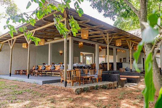 An expansive, modern open-air lounge at Adrift River Club with wooden pallet seating, gray cushions, and soft lantern lighting under a high timber roof.