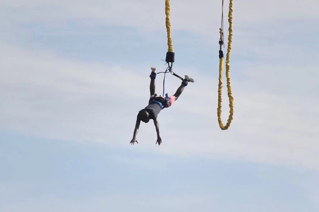 A silhouetted jumper mid-air during a bungee jump over the Nile, suspended by a yellow cord against a vast, clear sky.