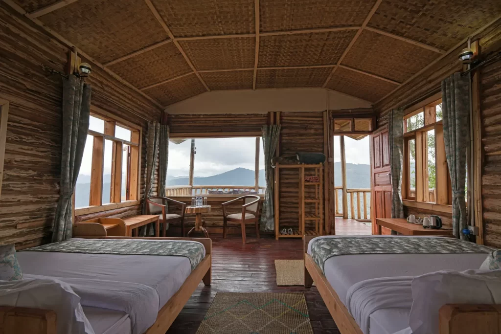 Kiram twin cabin interior at Bwindi Orugano Lodge showing wooden log walls woven bamboo vaulted ceilings and large windows facing the valley