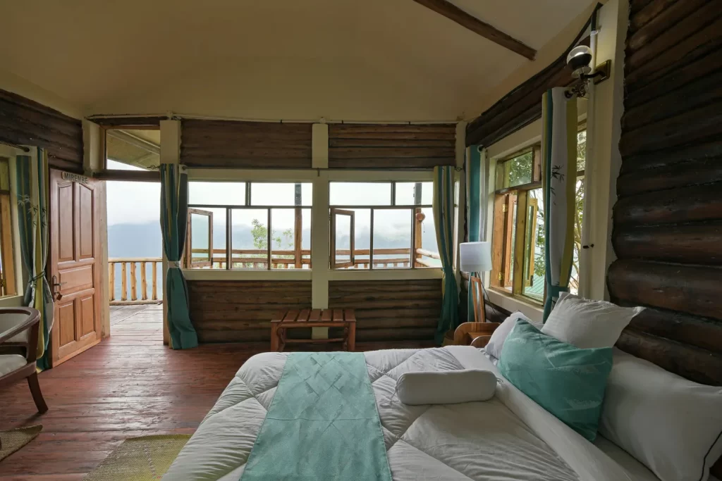 Mirembe cabin bedroom at Bwindi Orugano Lodge with a double bed teal accents and glass doors opening to a private veranda with mountain views