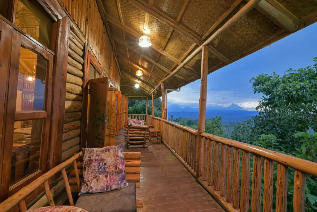 Wide wooden veranda at Bwindi Orugano Lodge with woven bamboo ceilings and timber seating overlooking the Virunga mountains at dusk
