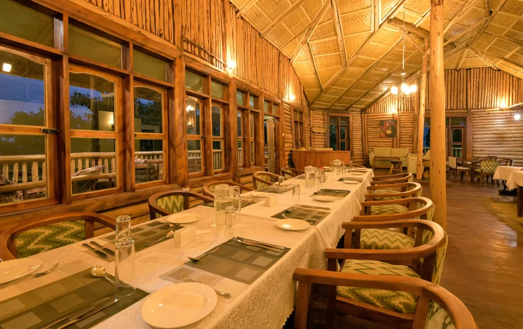 The main dining room at Bwindi Orugano Lodge featuring long clothed tables wooden chairs warm indoor lighting and woven bamboo ceilings