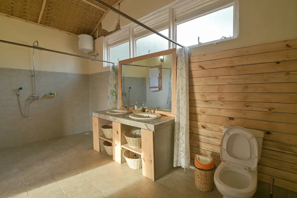 En-suite cabin bathroom at Bwindi Orugano Lodge with double sinks a large mirror a tiled shower area and wood-panelled walls