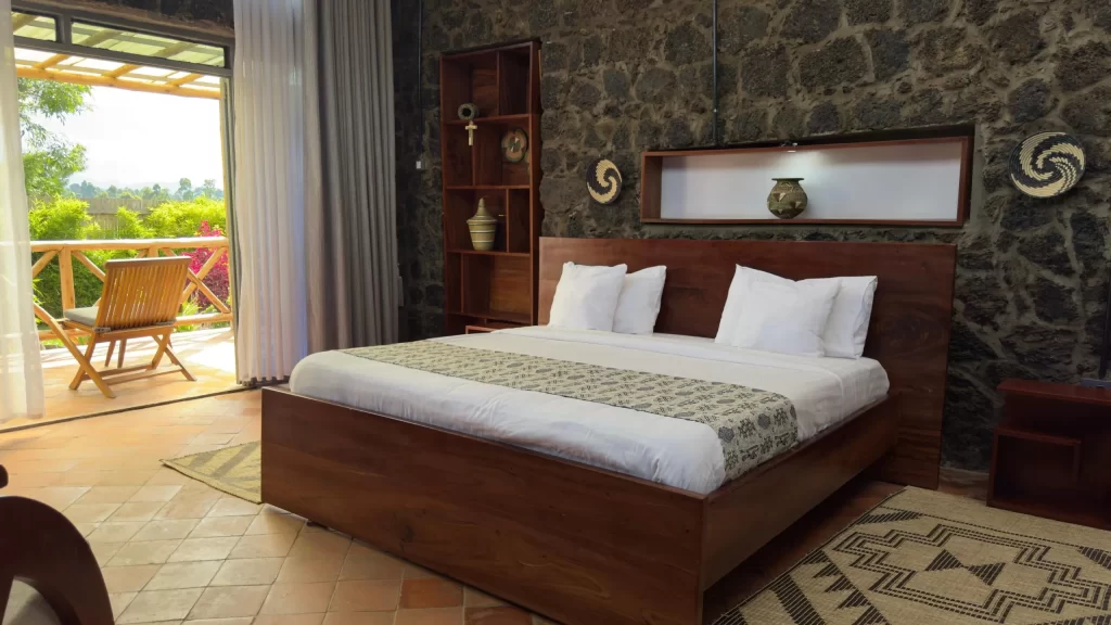 Imbogo Diners and Lounge luxury executive suite interior showing a king bed against volcanic stone walls, terracotta floors, and an open balcony door