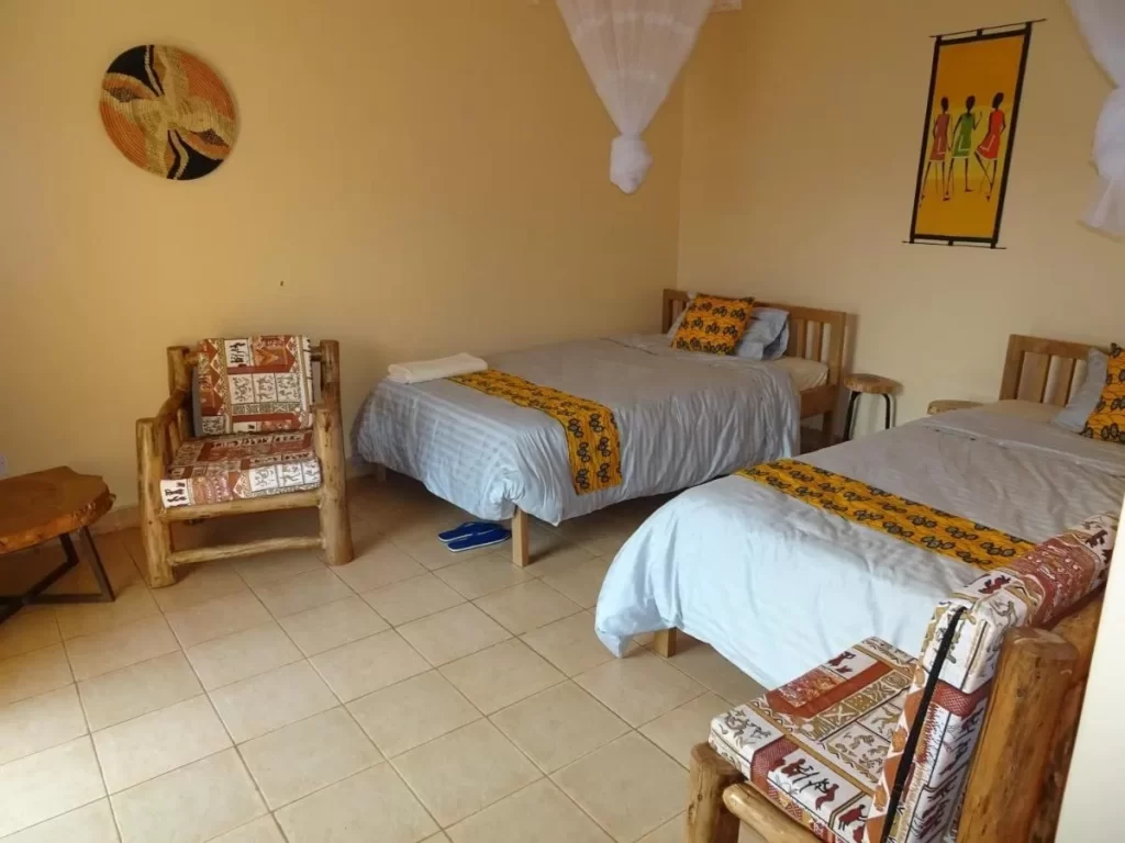 A clean, brightly lit twin bedroom at Lycklama Guest House with wooden bed frames, mosquito nets, and vibrant African-print textiles and wall art.