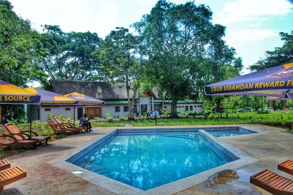 A crystal-clear geometric swimming pool reflecting the sky, surrounded by rustic wooden loungers and the lush, deep greenery of the Kalagala forest canopy.