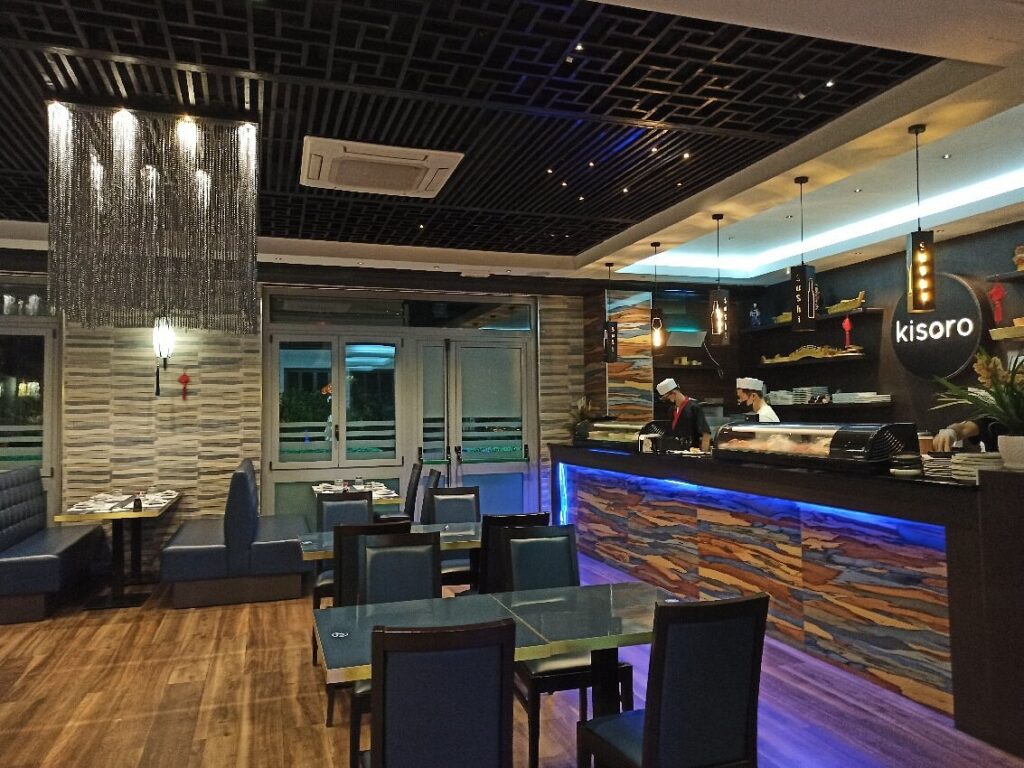 Modern restaurant interior in Kisoro with a sleek sushi bar counter, blue LED lighting, indoor seating tables, and contemporary design elements.