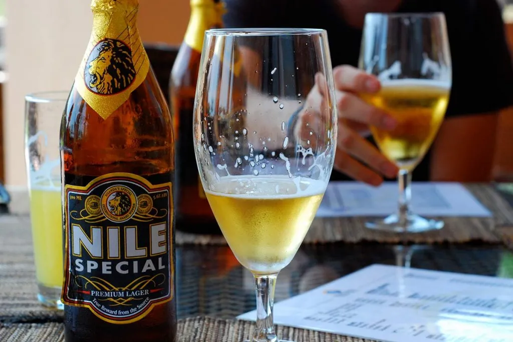 A condensation-covered bottle of Nile Special Premium Lager next to a partially filled glass, capturing the golden glow of a perfect riverside sundowner.