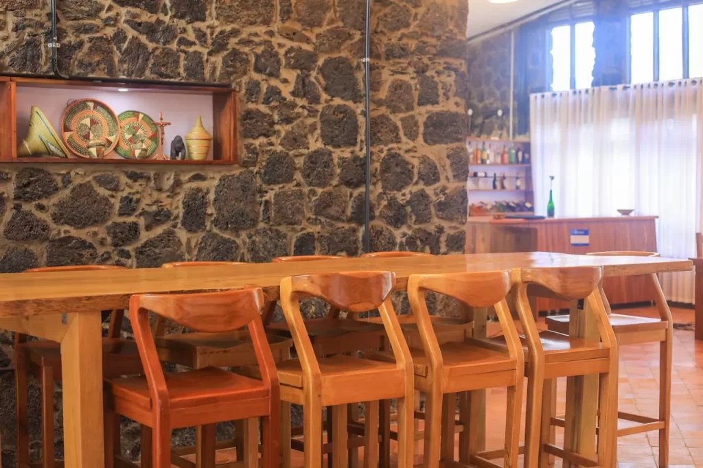 Imbogo Diners and Lounge indoor bar area featuring a long wooden table, custom high chairs, and a volcanic stone wall