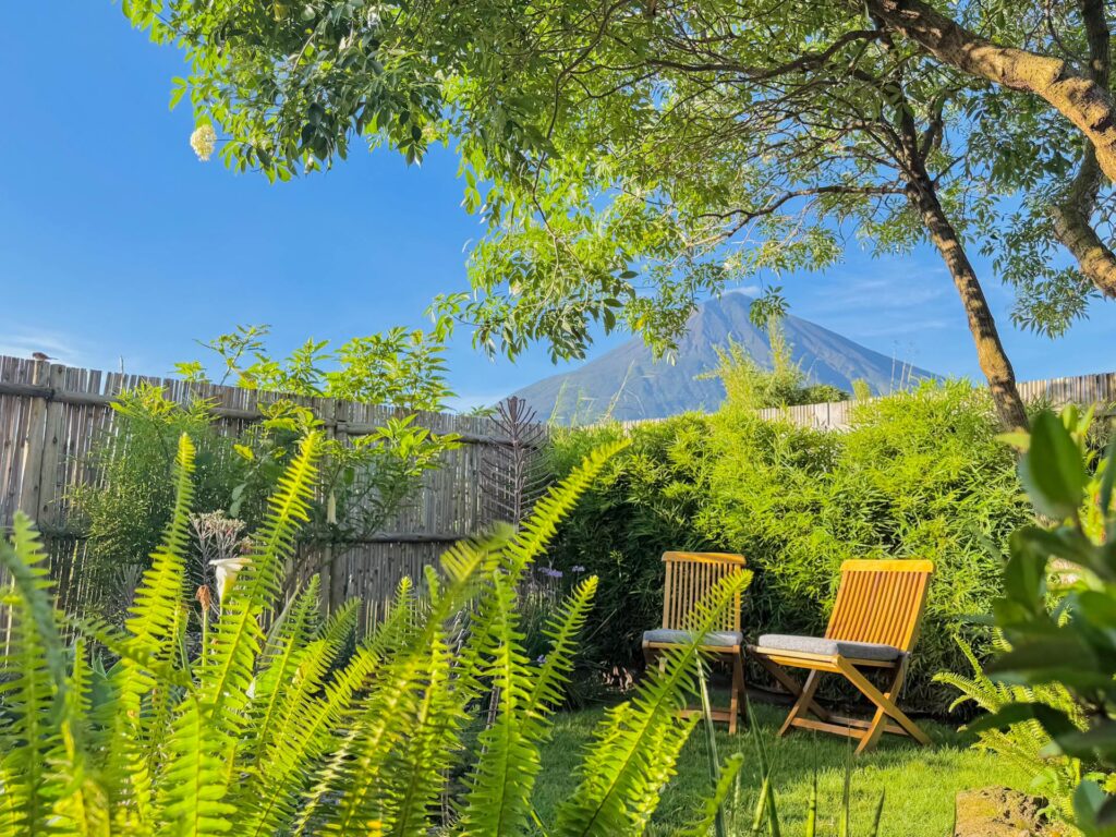 Imbogo Diners and Lounge landscaped garden with wooden chairs framing a clear view of Mount Muhabura volcano peak in Kisoro Uganda