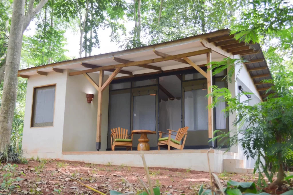 A minimalist eco-cottage with a wide wooden porch and outdoor seating, nestled quietly among tall trees at Adrift River Club.