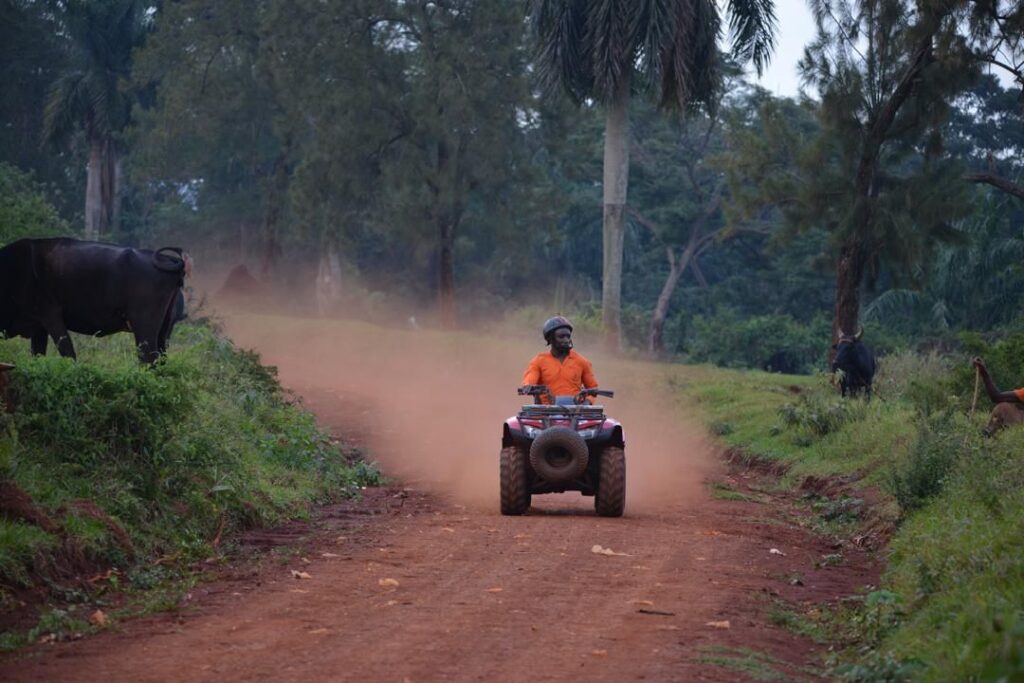 Nyege Nyege 2026 Guide A person riding a red quad bike on a dusty dirt road through a rural area in Jinja.