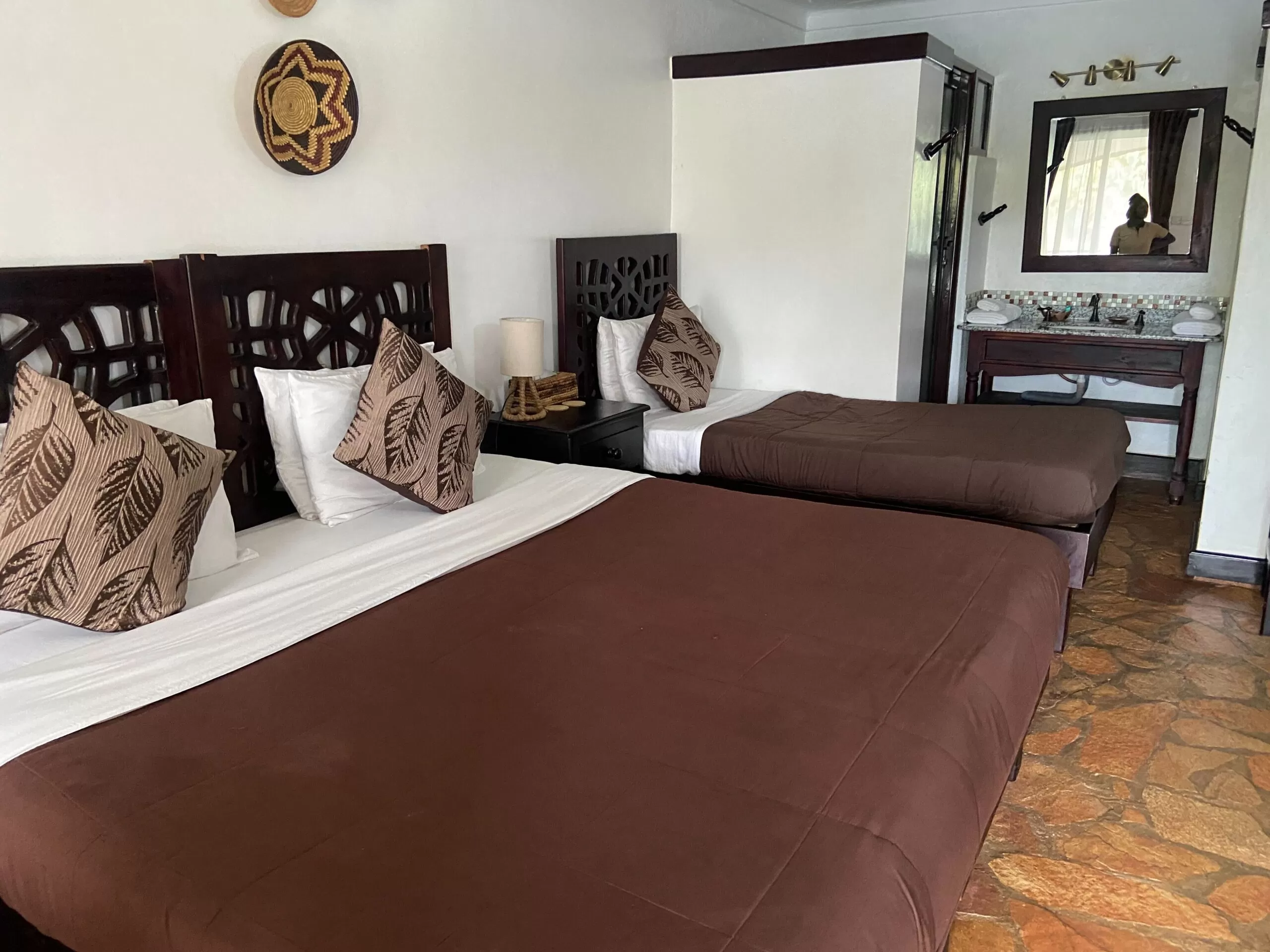 Nyege Nyege 2026 Guide A luxury guest room at Nile River Bend featuring large beds with brown linens and decorative wooden headboards.