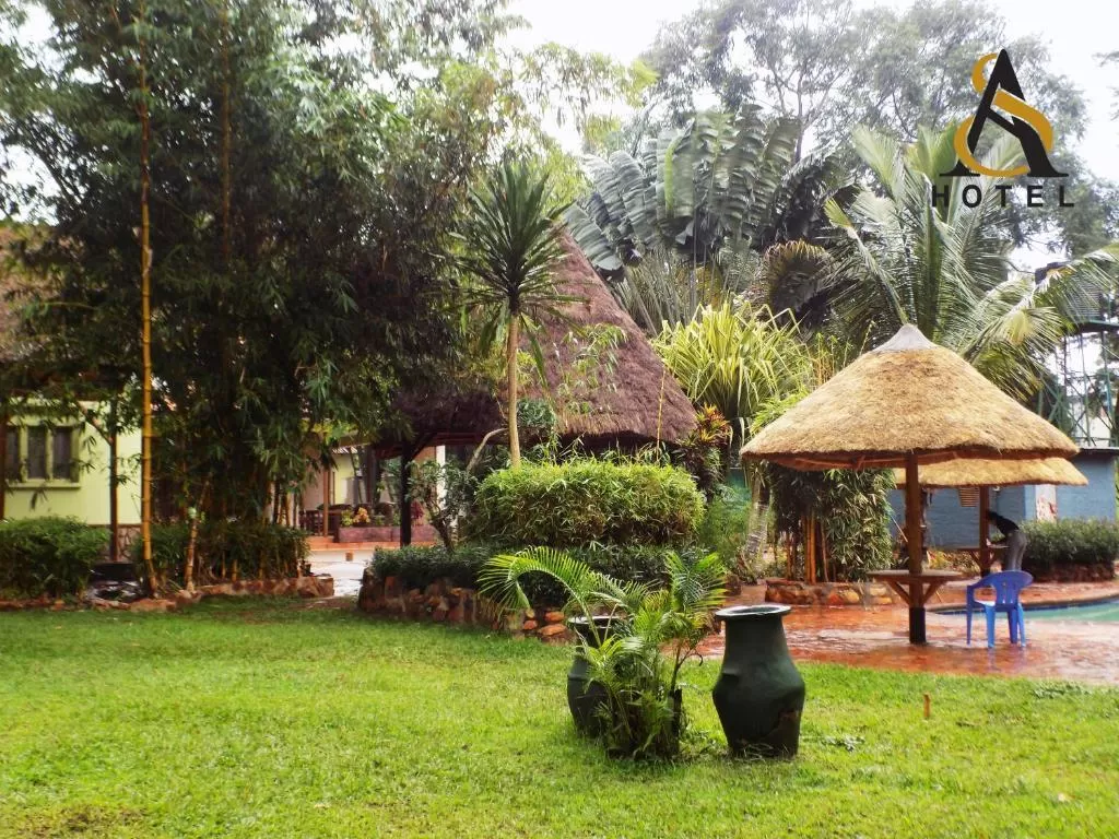 The lush green lawns, tropical foliage, and traditional thatched umbrellas at  Afro Smiles Hotel & Guest House.