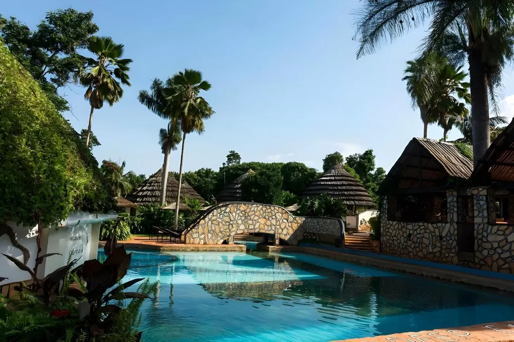 The stone-bridge swimming pool surrounded by palm trees and thatched cottages at Kingfisher Safaris Resort Hotel Jinja.