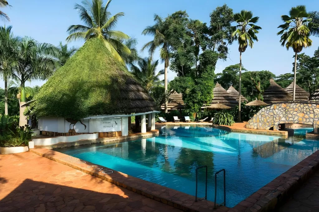 A sunny daytime view of the stone-bridge swimming pool and surrounding thatched cottages at Kingfisher Safaris Resort Hotel Jinja.