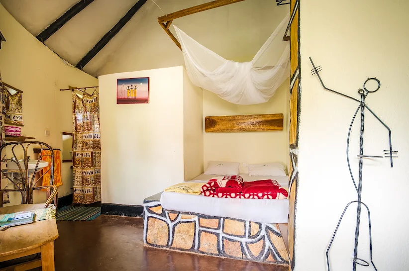 A standard room interior with a stone platform bed, mosquito net, and traditional craft details at Kingfisher Safaris Resort Hotel Jinja.