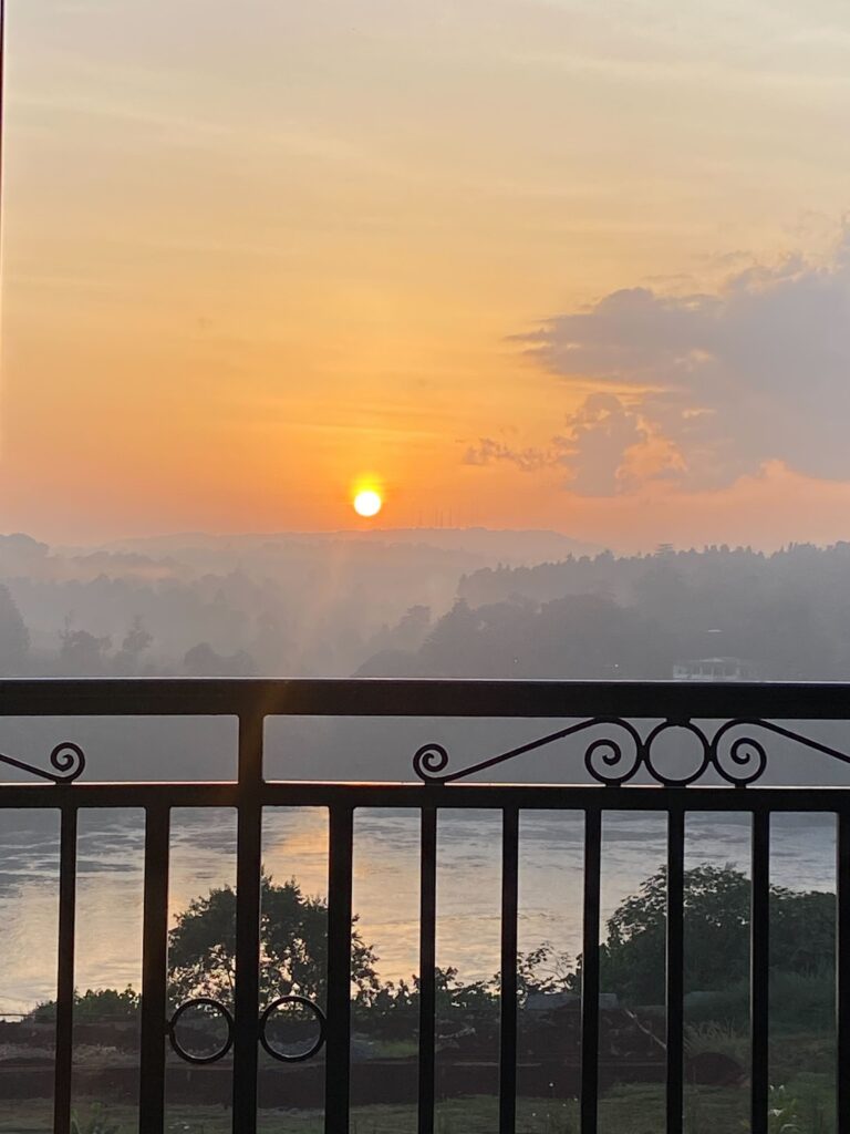 Sunset view over the River Nile in Jinja framed by the iron balcony railing of Mountain Inn Resort with hills in silhouette