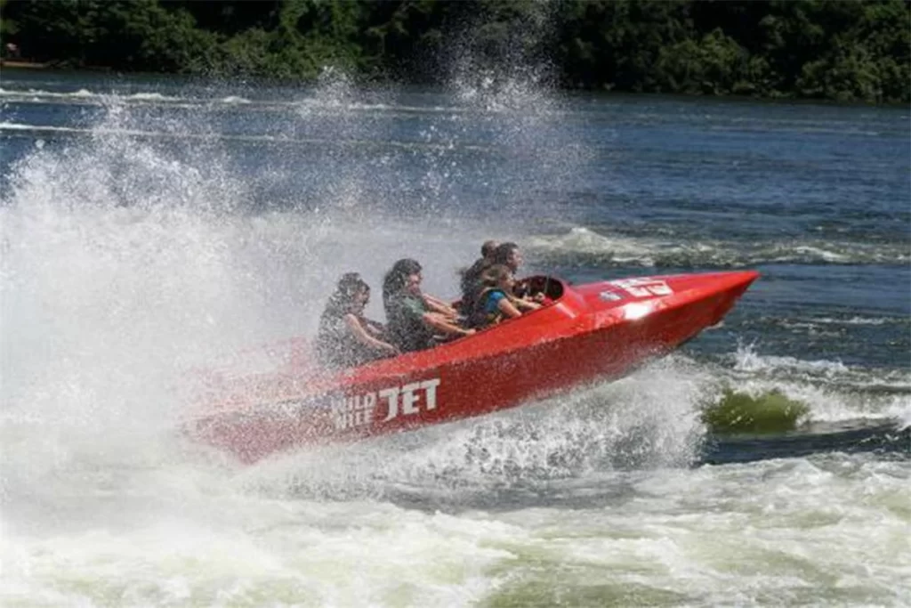 A high-speed red jet boat splashing water through rapids during an adventure excursion on a Jinja Uganda itinerary