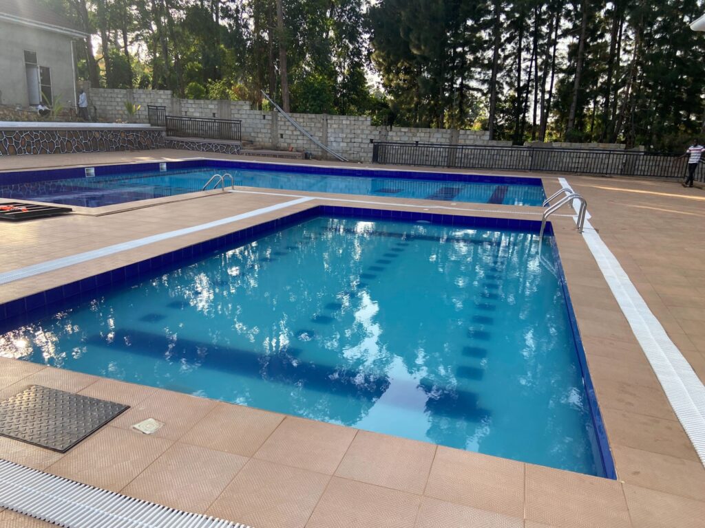 Main outdoor swimming pool at Mountain Inn Resort Jinja surrounded by tall pine trees brick buildings and manicured green lawns at sunset