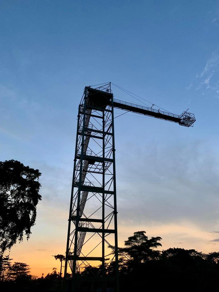 Bungee Jumping in Jinja: The Ultimate Guide to Uganda’s Adventure Capital The silhouette of a purpose-built steel tower used for bungee jumping in Jinja, featuring a long horizontal cantilever platform extending over the tree line against a vibrant orange and blue sunset sky.