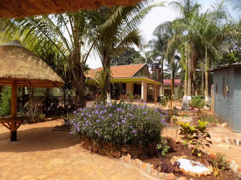 A beautifully landscaped stone courtyard featuring a central stone planter filled with purple flowers, surrounded by tall palm trees and thatched gazebos at Afro Smiles Hotel & Guest House.