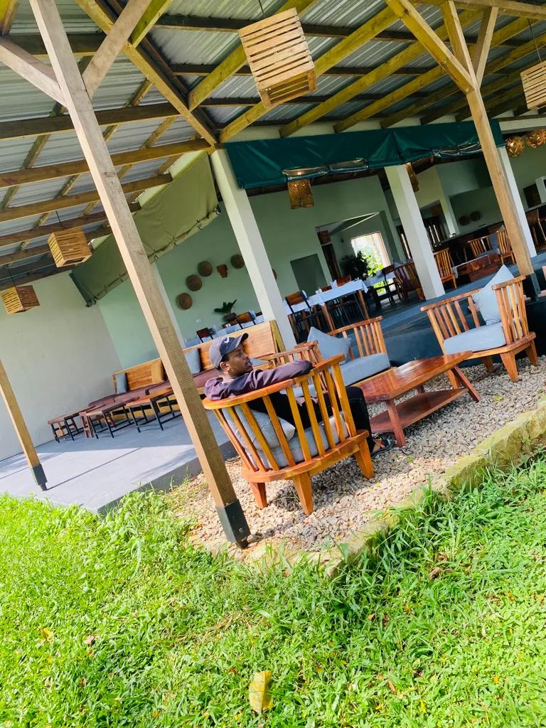 Bungee Jumping in Jinja: The Ultimate Guide to Uganda’s Adventure Capital A man relaxes in a wooden armchair at an open-air resort lounge featuring rustic wooden beams, gravel flooring, and hanging box lanterns, showcasing a peaceful accommodation option for where to stay in Jinja.