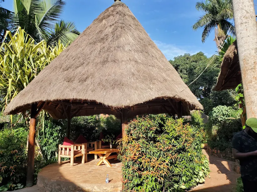 A large outdoor thatched gazebo lounge featuring heavy timber armchairs, red cushions, and a wooden coffee table in the tropical garden at Afro Smiles Hotel & Guest House.