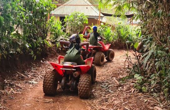 Riders  wearing a helmet and protective overalls sits on an ATV at a mud-covered track heading out for quad biking in jinja Uganda.