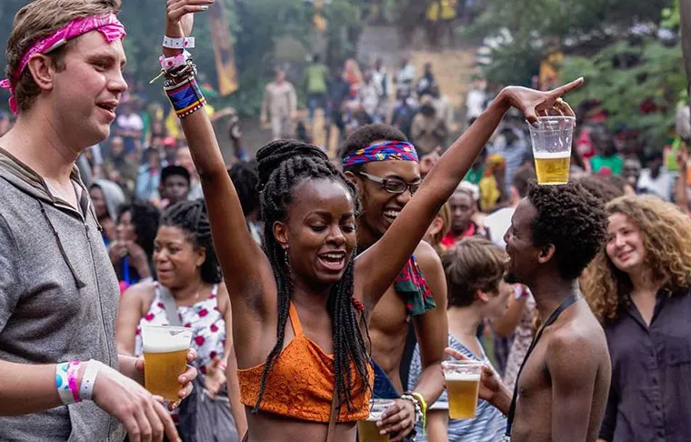 A lively, diverse crowd of festival revellers dancing outdoors with drinks raised at the Nyege Nyege festival in Jinja Uganda in the Nyege Nyege 2026 survival guide
