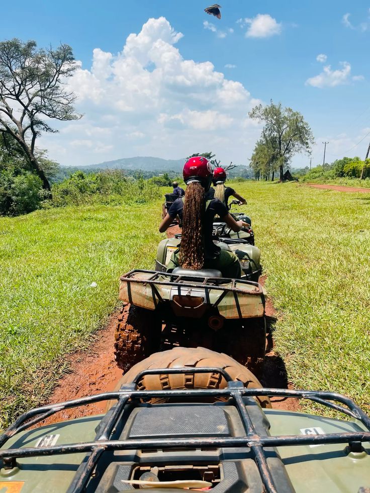 A group of travelers riding all-terrain vehicles in a line down a muddy dirt track through green grass fields, capturing the trail experience of quad biking in jinja uganda.