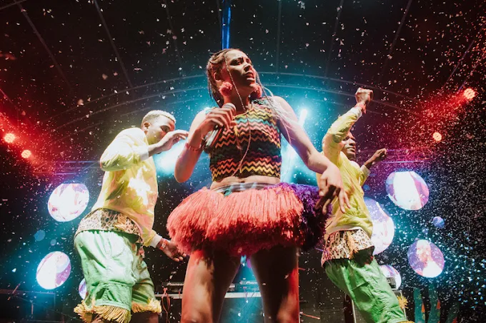 A female musical artist performing live on stage surrounded by confetti shower and backup dancers in colorful outfits at Nyege Nyege festival in Jinja Uganda.